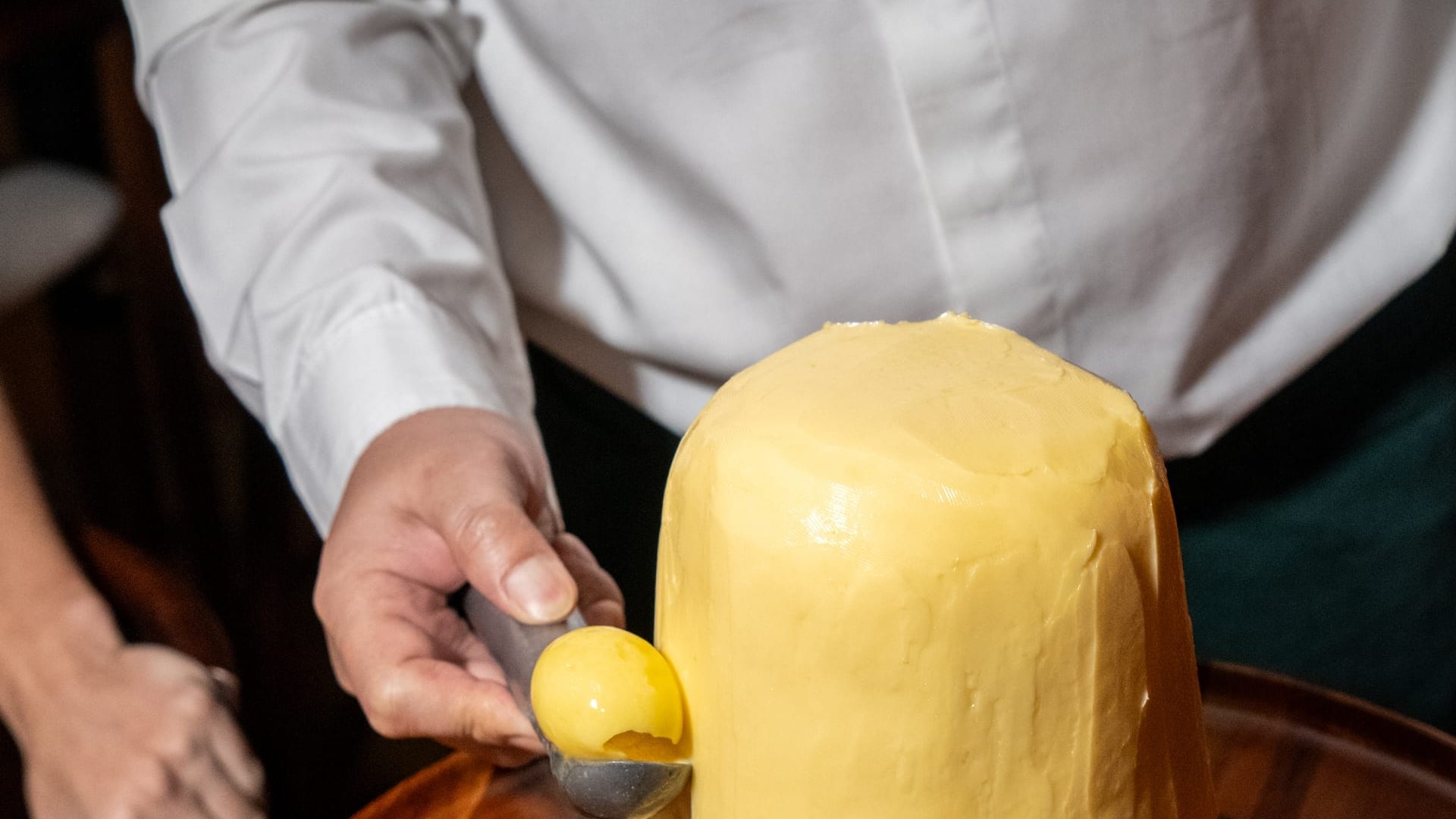A whole block of French butter on a wooden board at Bisou Bangkok, a curl being scooped from it with a warm spoon