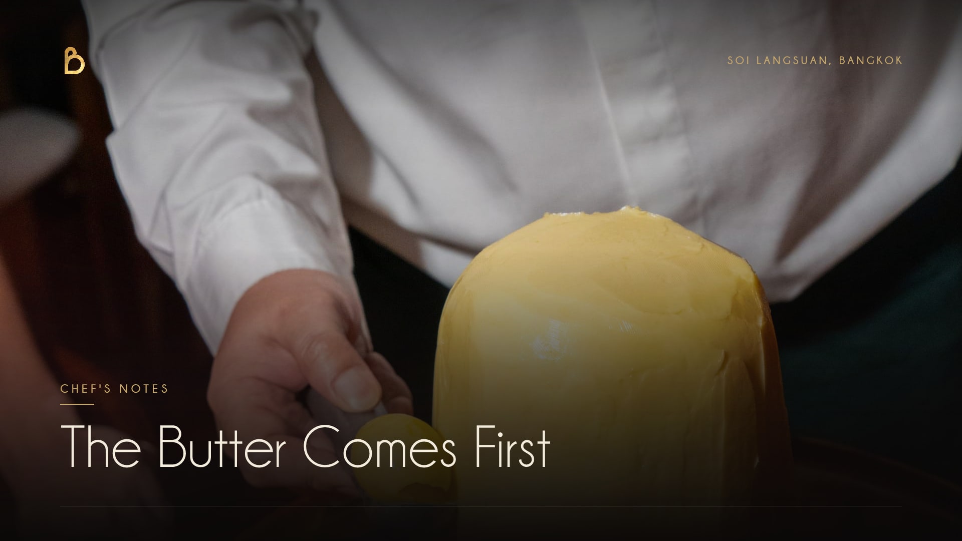 A whole block of French butter on a wooden board at Bisou Bangkok, a curl being scooped from it with a warm spoon